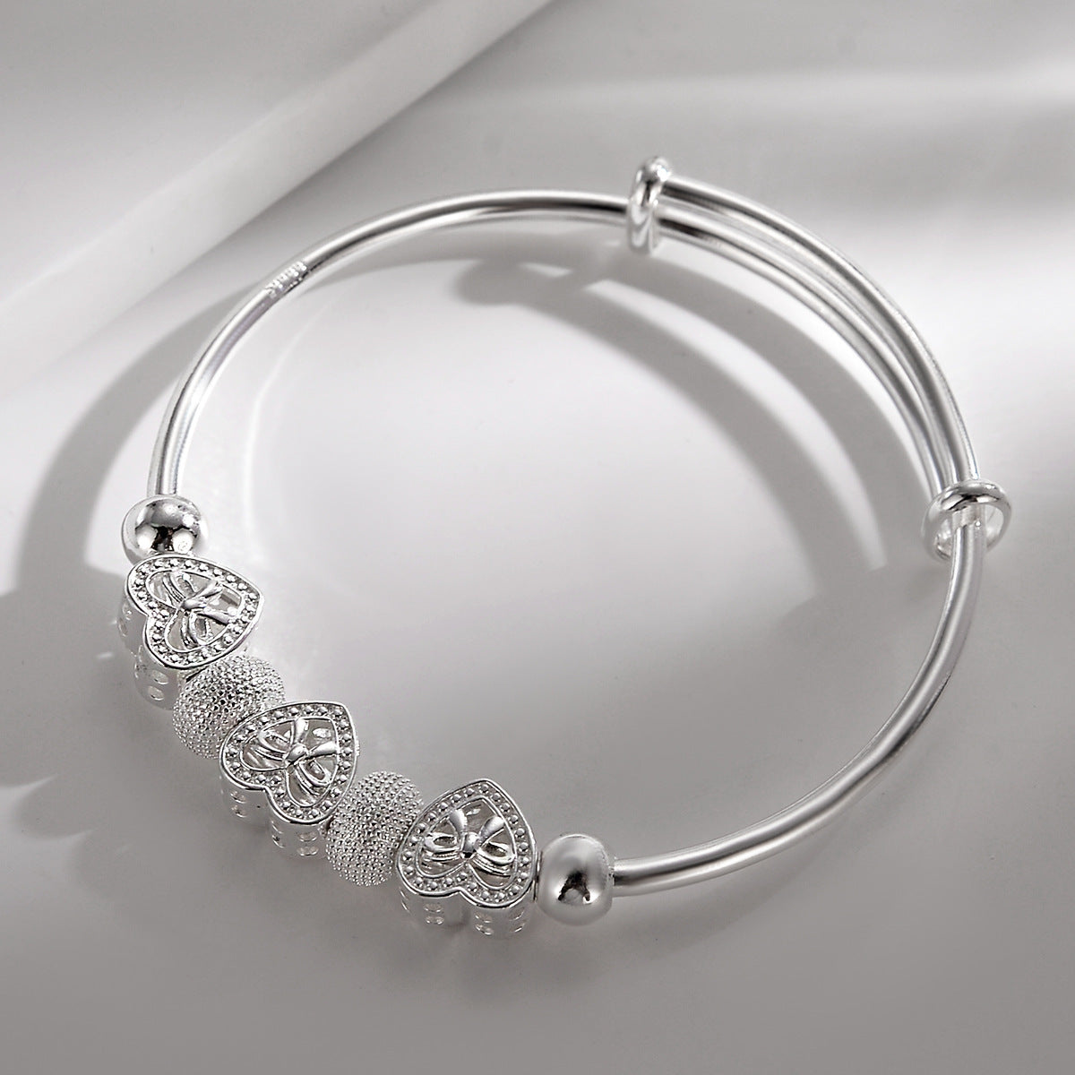 Heart Charm Bangle shown on a soft grey background, with its sliding adjustable closure